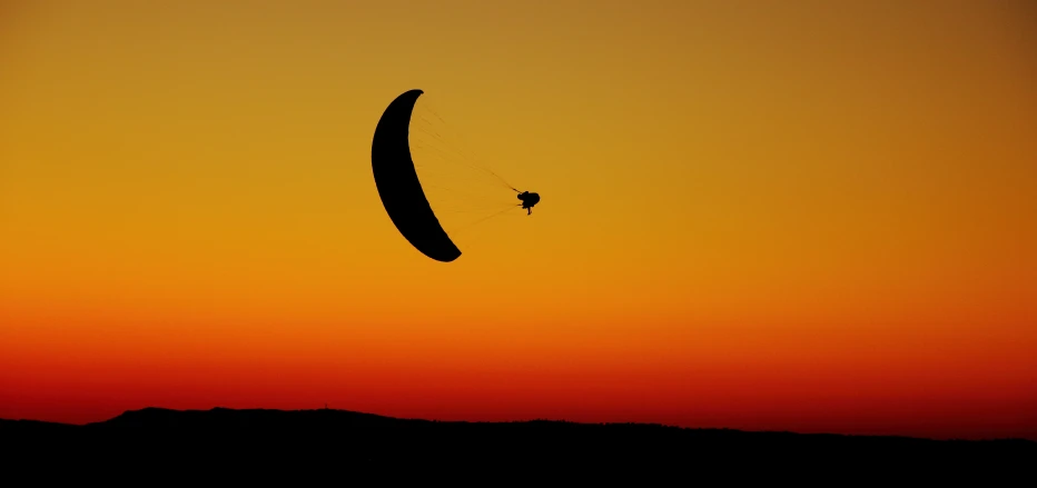 the sun sets behind an empty paraglider