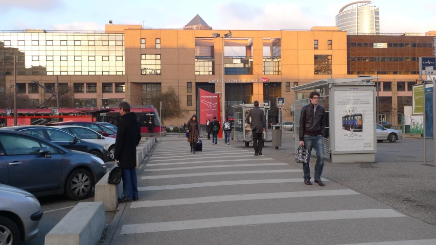 a street with cars and pedestrians, several are leaving the building