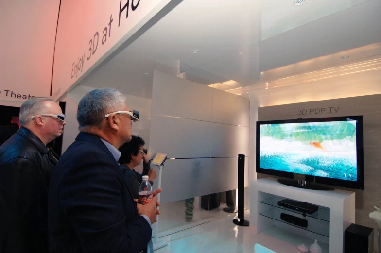 men in suits look at a flat - screen television while two others are looking on