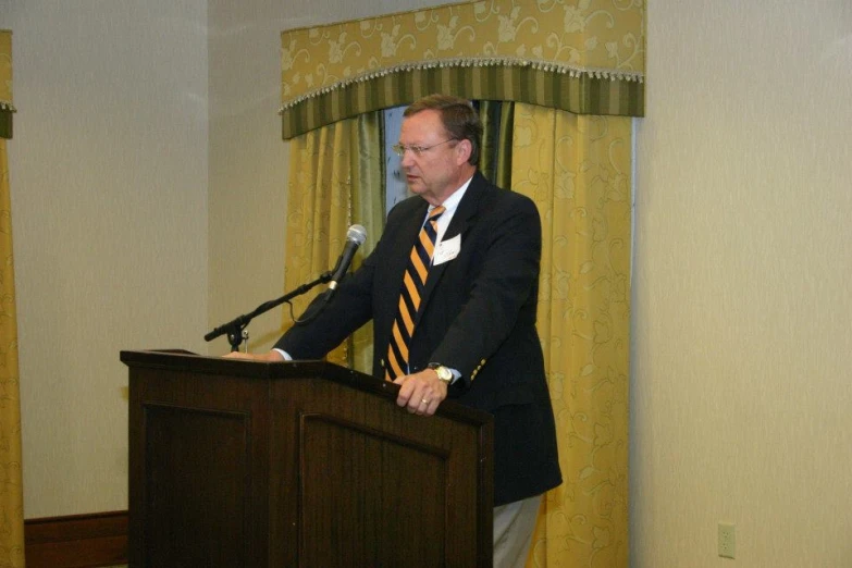 a man in a suit and tie stands behind a podium, giving a speech