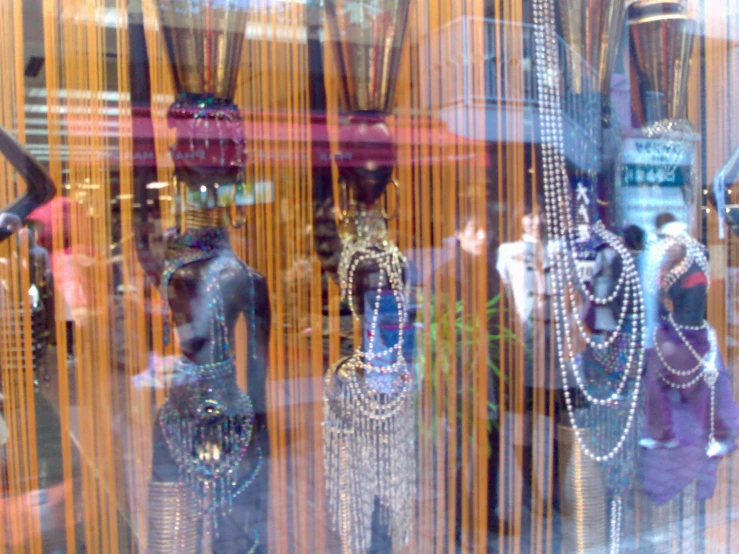 many mannequins wearing costumes and necklaces are behind glass