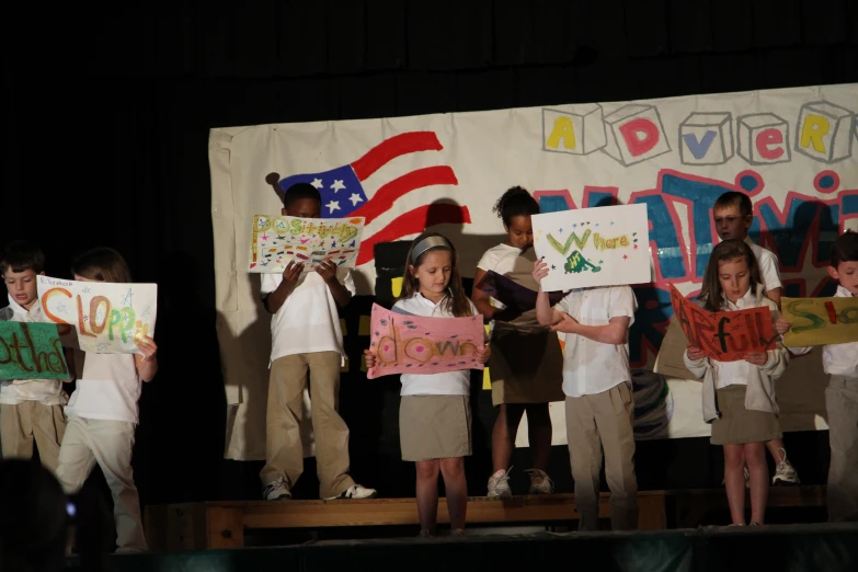 young children holding signs with american flag on stage