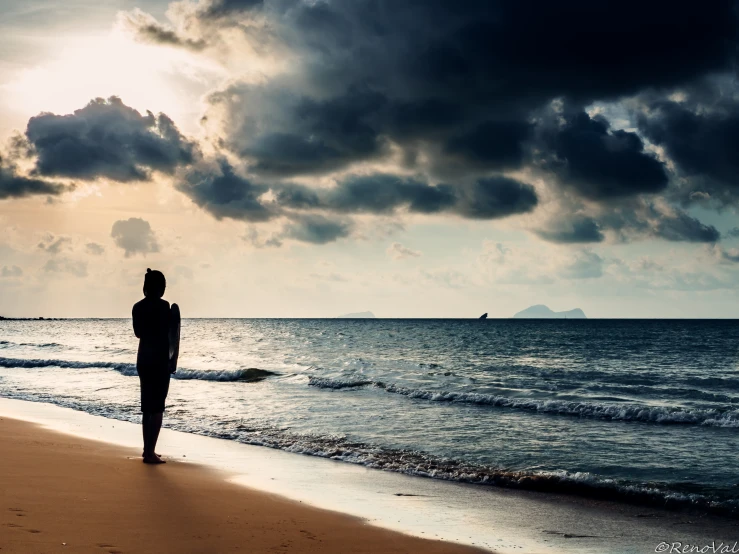 a woman walks alone on the beach at sunset