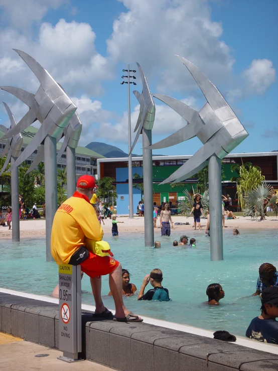 man and child at the edge of a blue pool as other people swim