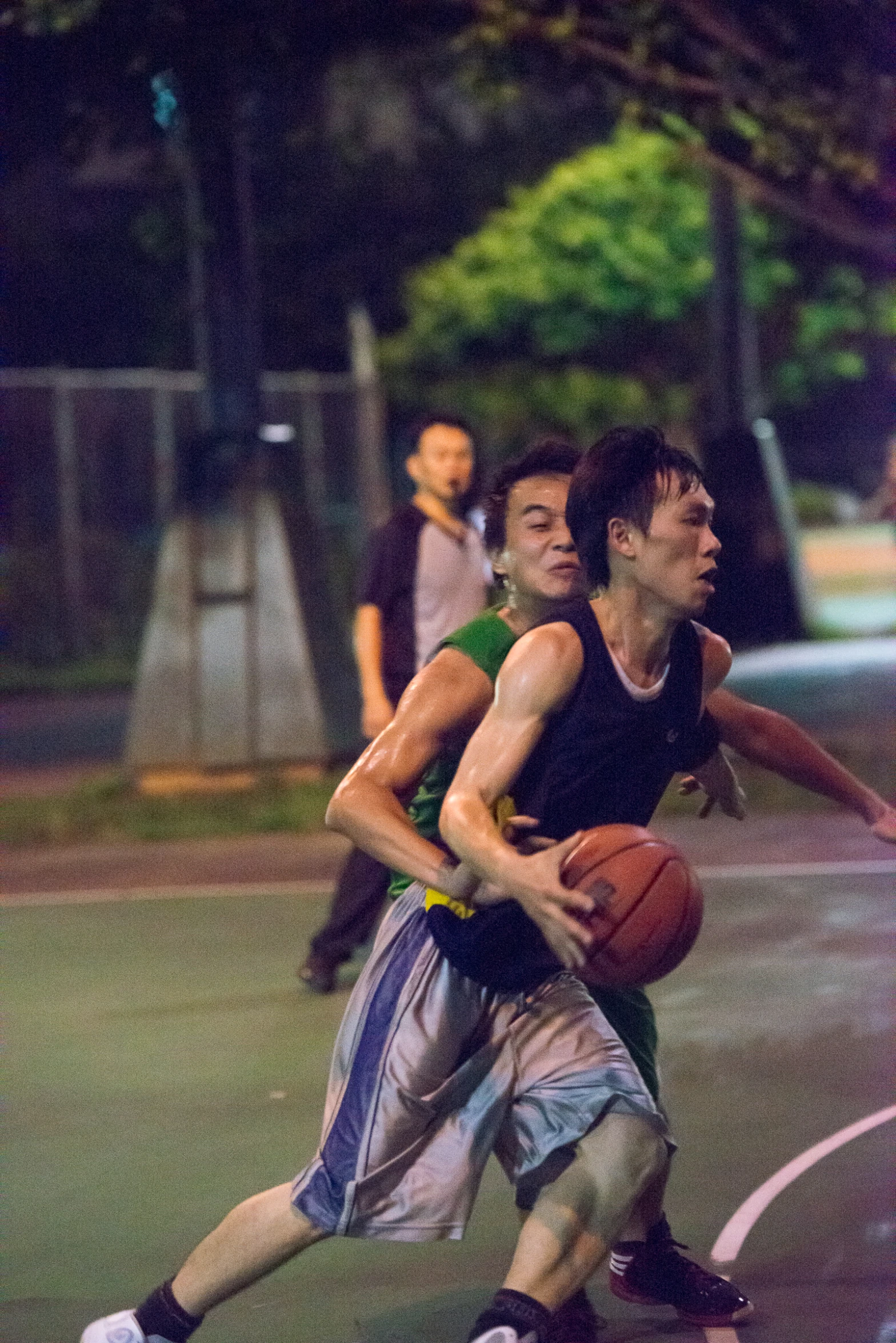 two young men in basketball gear playing basketball on a court at night