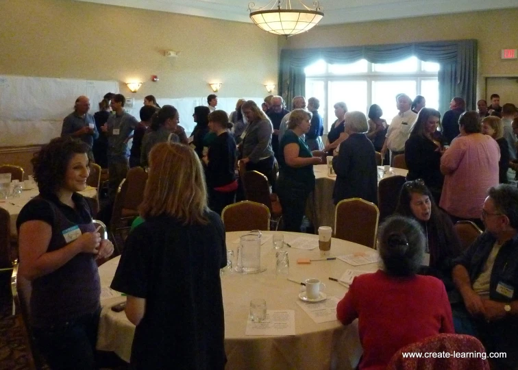 several people are standing around the tables in a room with white clothed tables