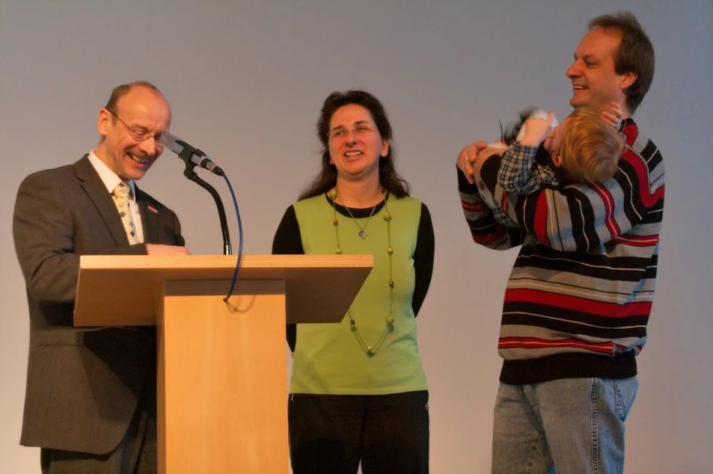 two adults standing near microphones playing a game with a toddler