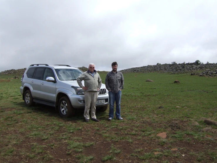 two people stand beside an suv on a green field