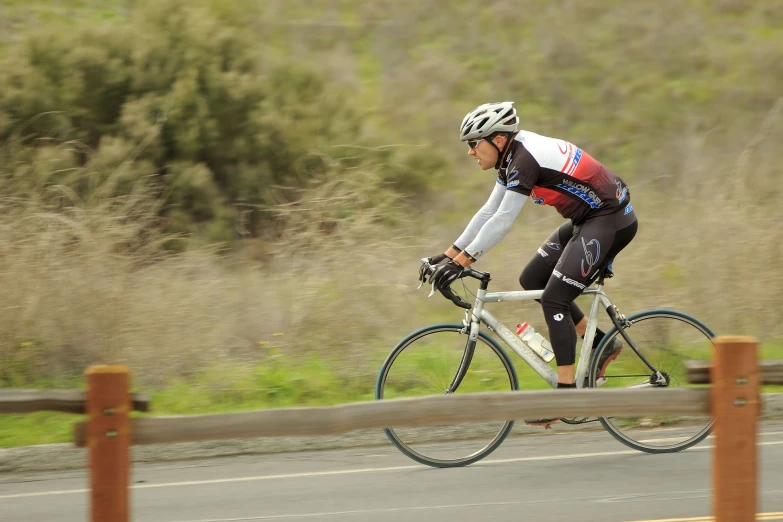 a man riding a bicycle down a road past tall grass