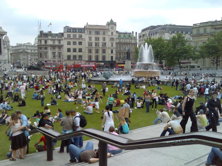 a crowd of people standing and sitting on grass next to buildings