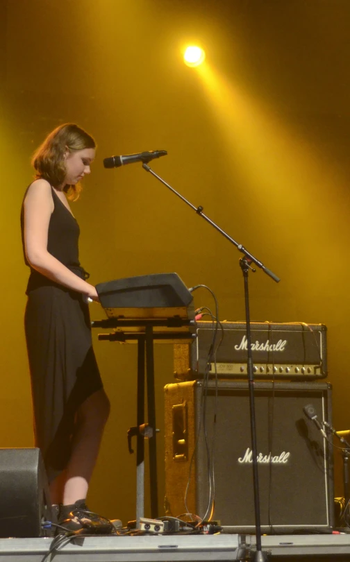 a woman standing at a microphone with a set of keyboards