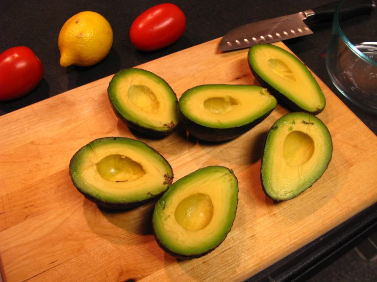 an avocado cut in half sitting on a  board with other fruit and vegetables next to it