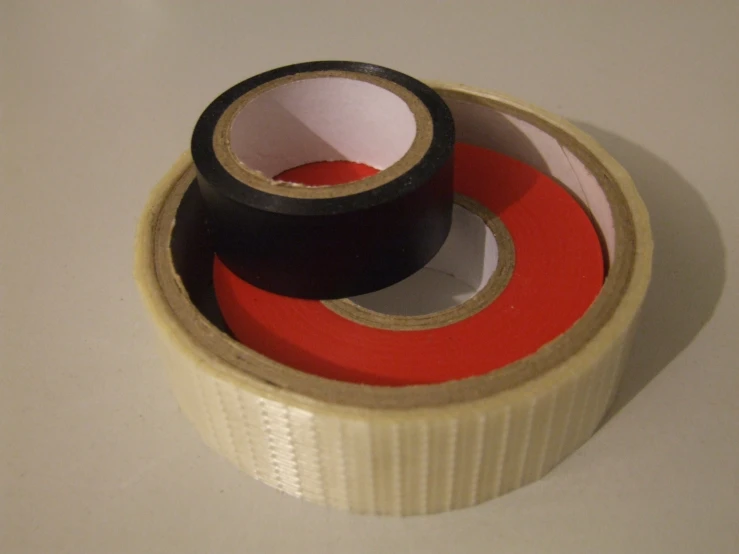 three rolls of black and red tape in a circle on a white surface