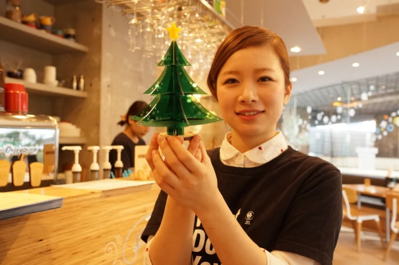 girl showing miniature christmas tree with candles at counter in cafe