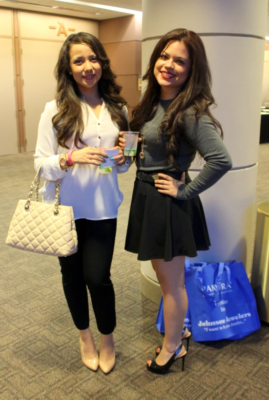 two woman standing next to each other holding purses