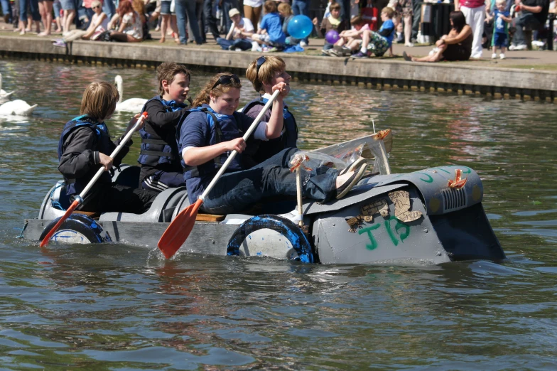 three people rowing a dragon boat with people standing nearby