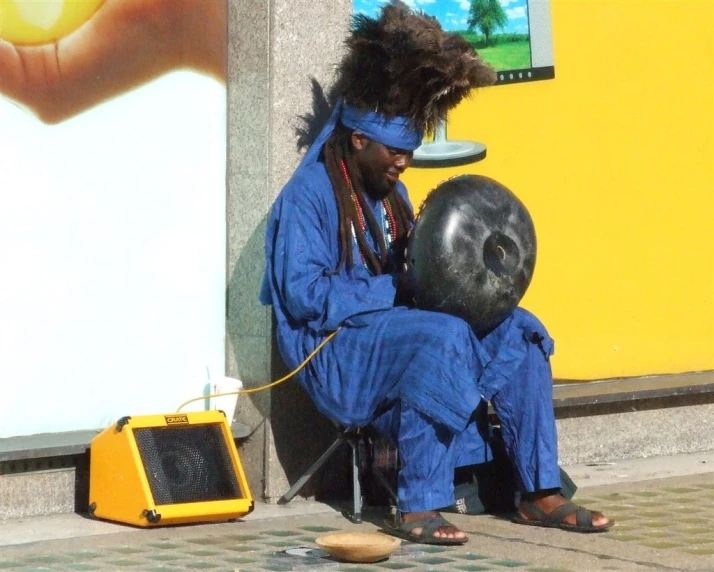a man with dreadlocks is on the street leaning against a wall with his cell phone