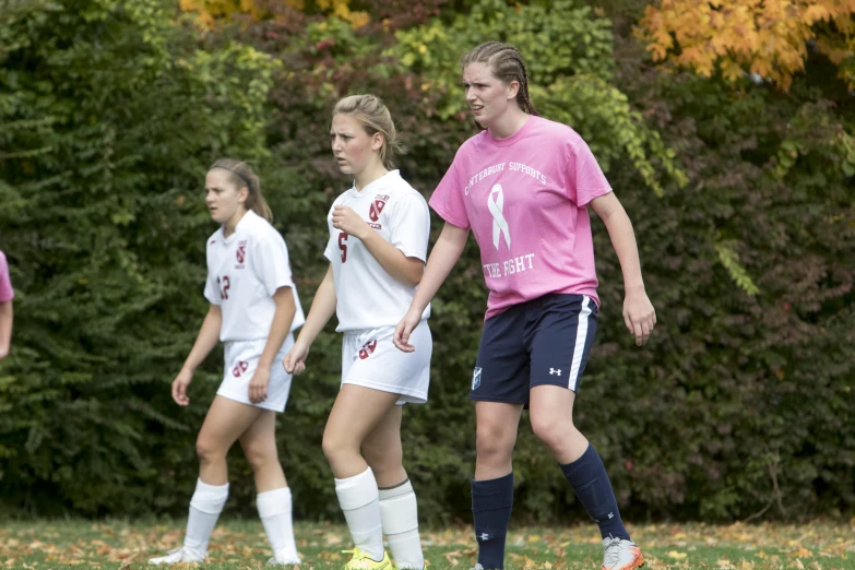 three girls are standing together as a soccer game goes on