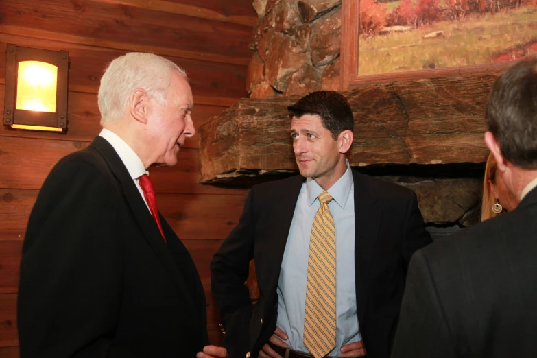 two men standing talking in front of a wooden wall