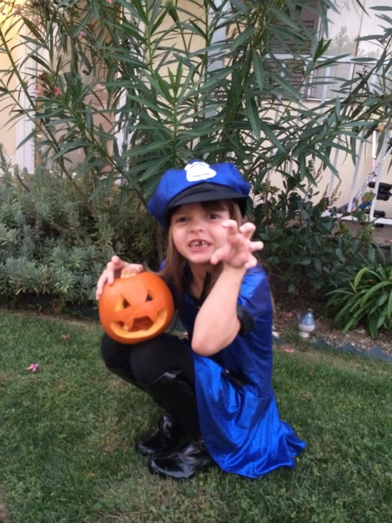 a  kneeling in the grass holding an orange jack - o'- lantern