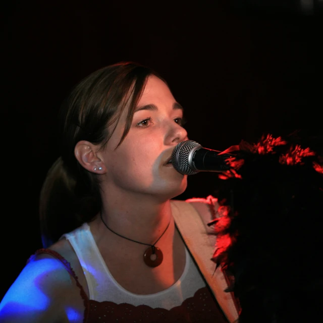 a woman singing into a microphone and holding a fan
