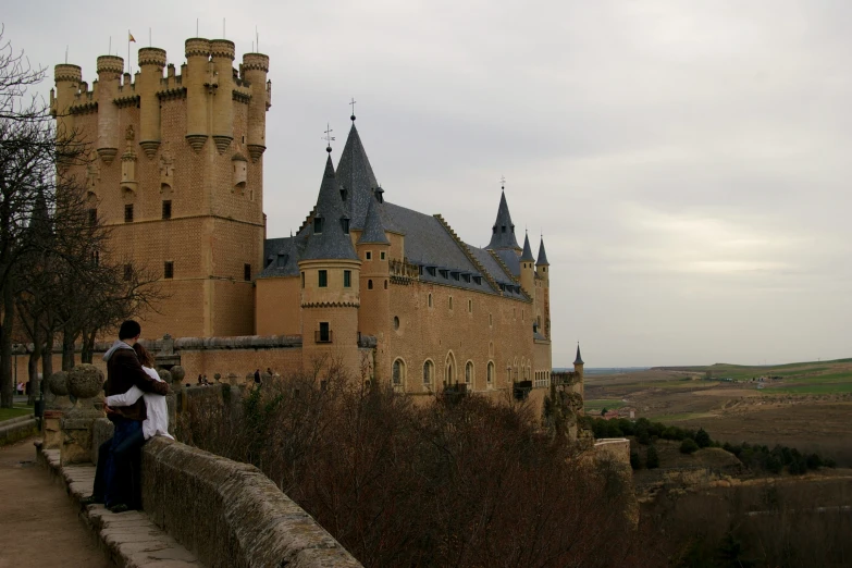 a couple standing on a bridge near a castle