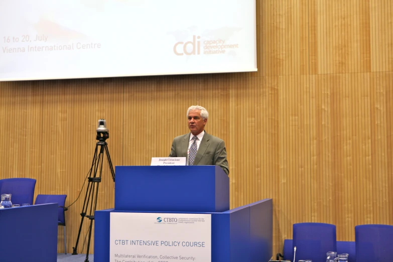 a man speaking at a podium with a video camera behind him