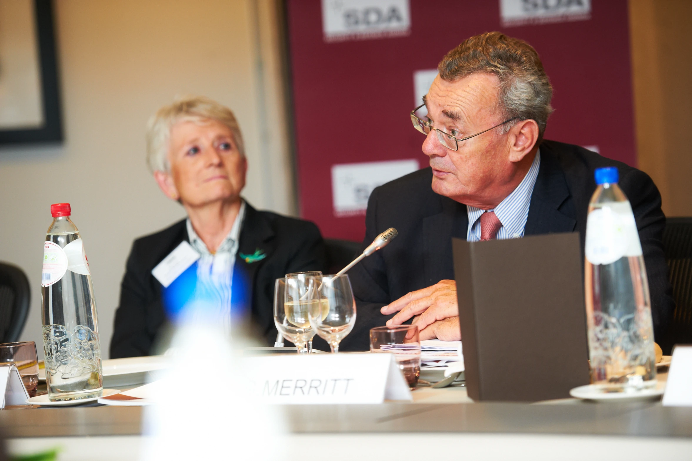 two older men sit at a table, looking at a sign