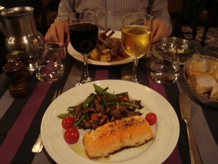 a person sitting at a table with a plate of food and glasses of wine