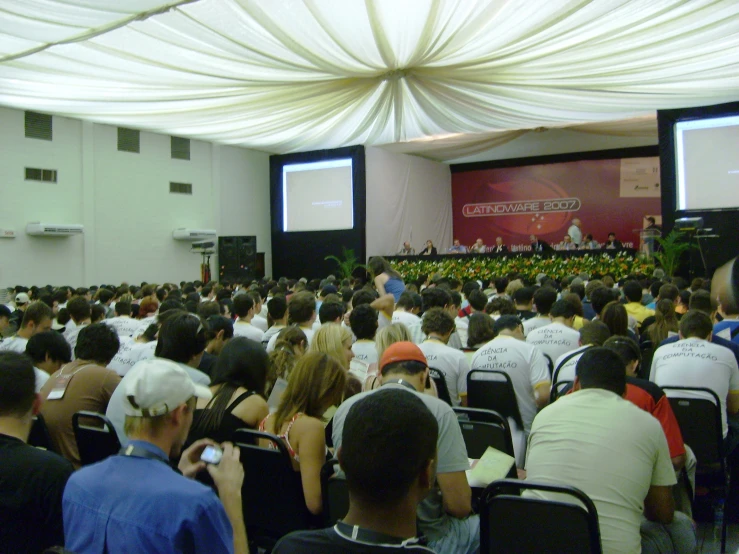 people in chairs watching an event on the large screen