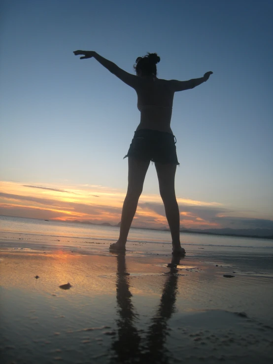a woman standing on a beach at sunset with her arms outstretched