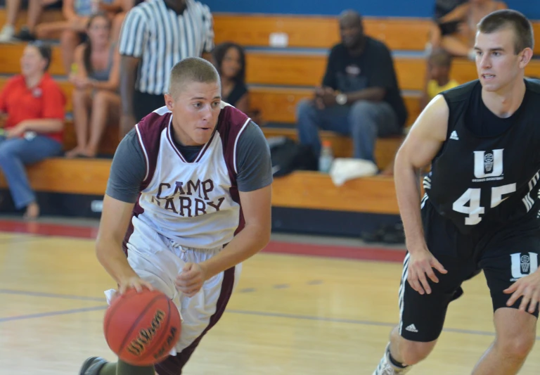 two men wearing black uniforms, one is on a basketball court while the other is running after the ball