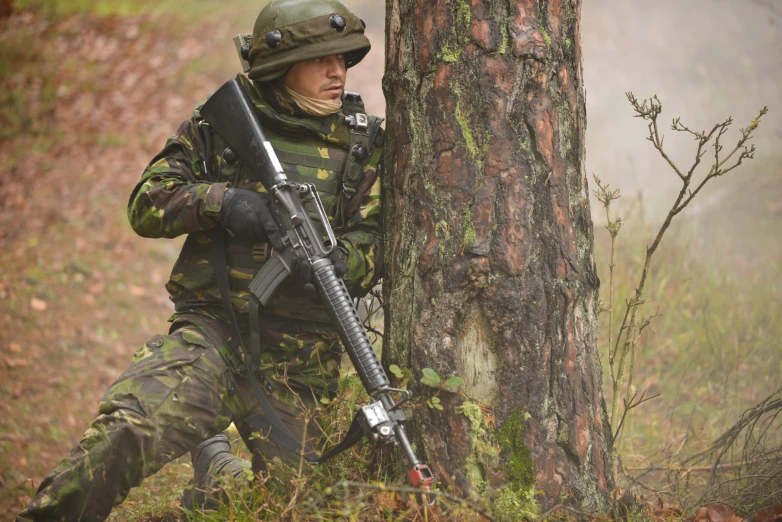 a man in camouflage holds a gun next to a tree