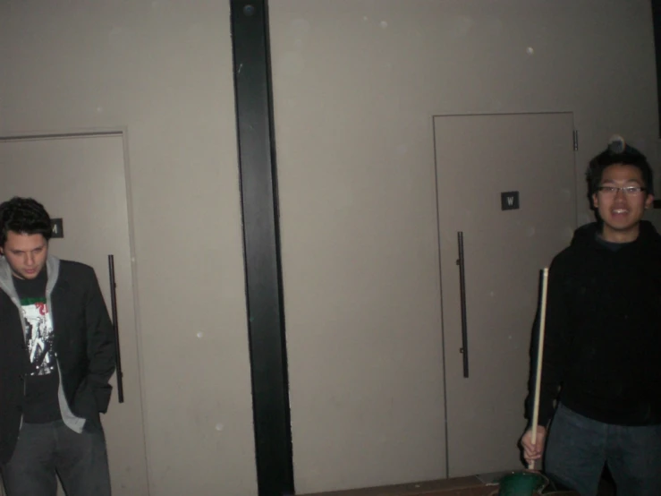 two men standing near the doorways in a room with a trash can and a garbage can