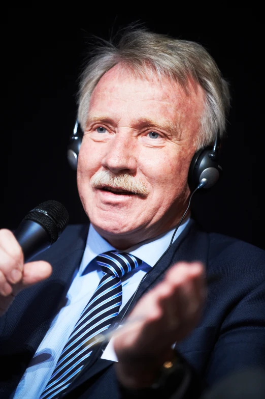 an older man talking into a microphone wearing headphones