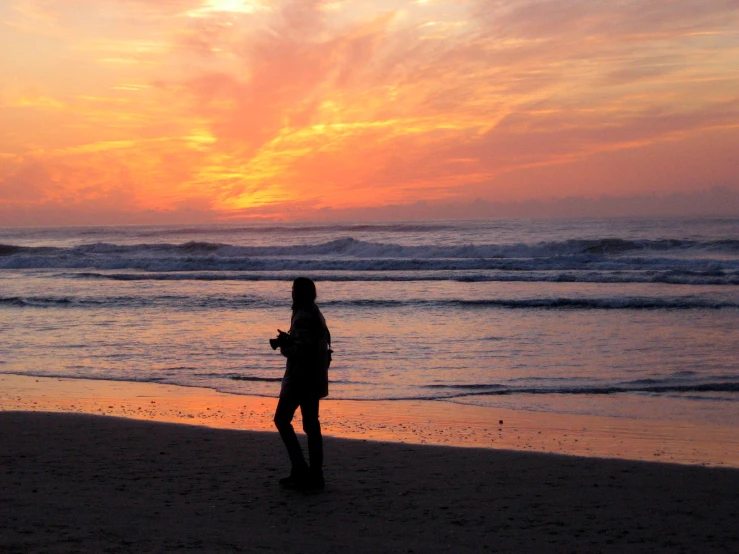 there is a woman standing on the beach at sunset