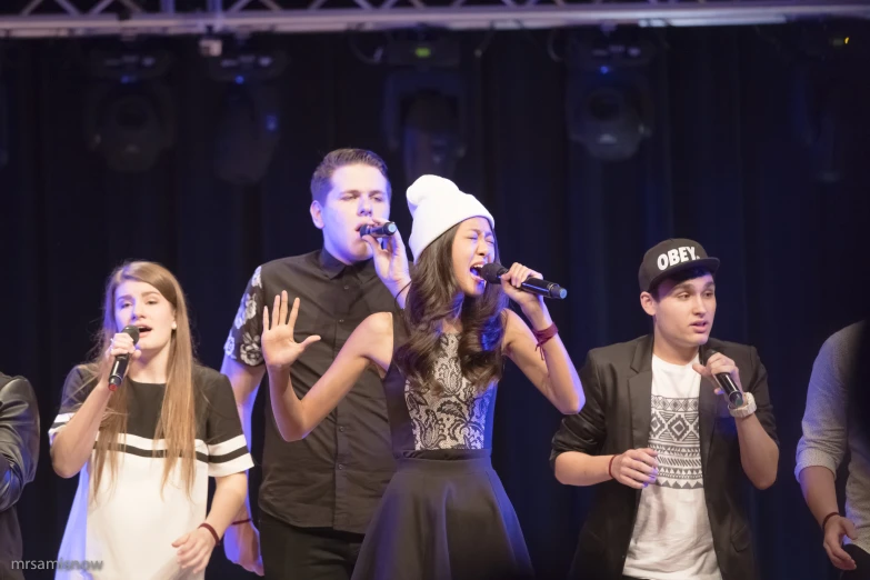 three adults sing with a young woman singing in front