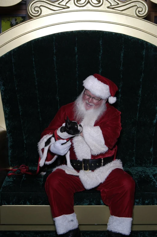 the santa is sitting on the green chair holding his cat