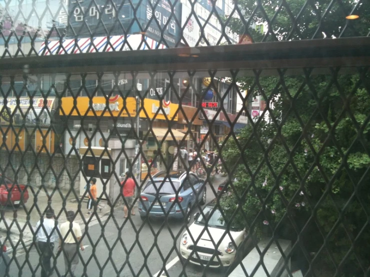 cars are driving on the street as viewed through a chain link fence