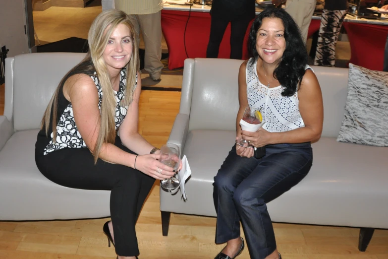 two woman sitting on grey couches posing for the camera