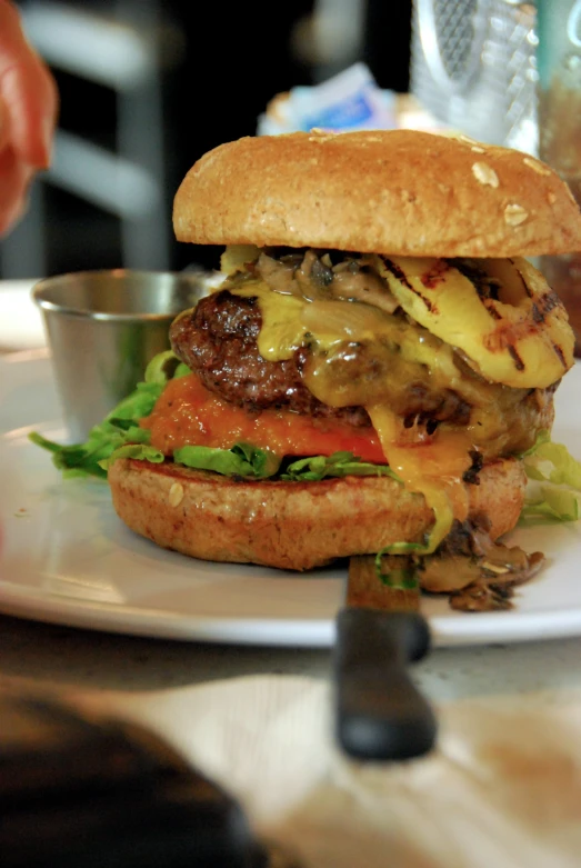 a hamburger sits on a white plate while someone holds their cell phone