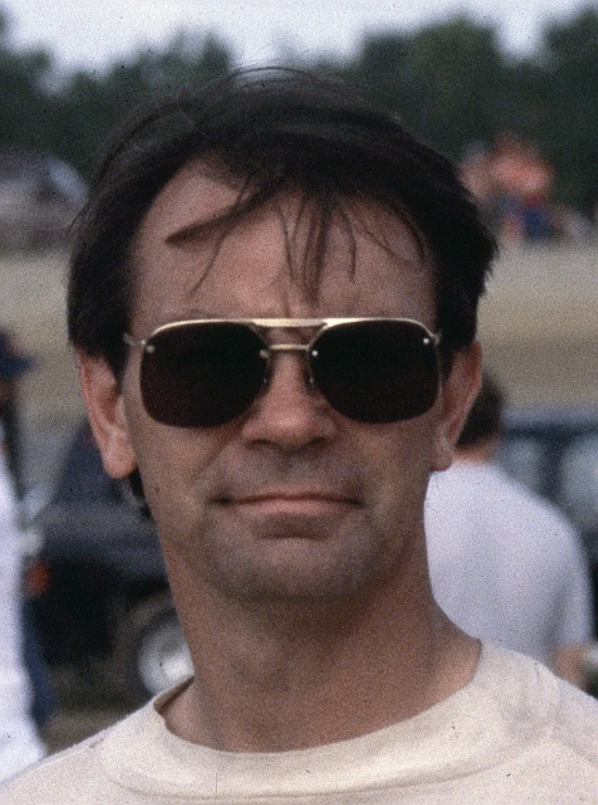 a man wearing sunglasses posing for a po in front of parked cars