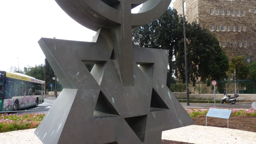 large gray sculpture near sidewalk with a bus passing by