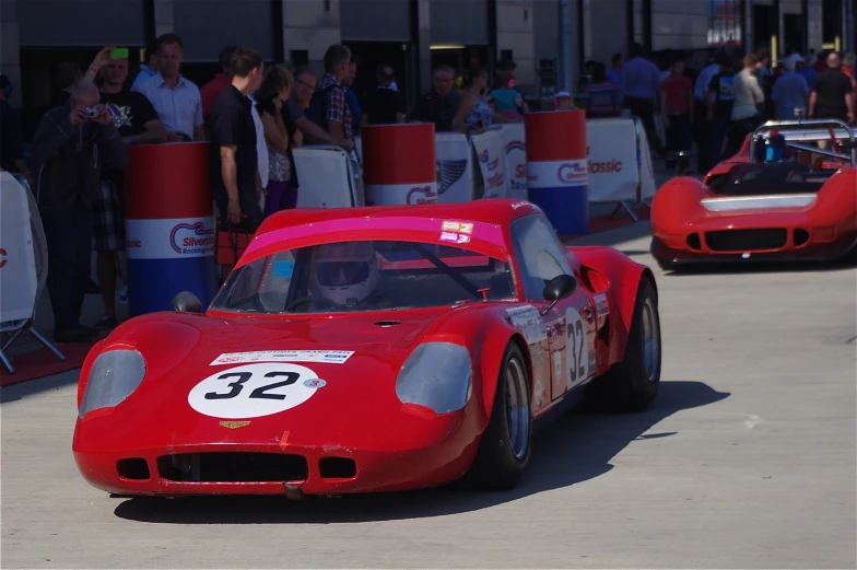 two red racing cars on a street with people watching