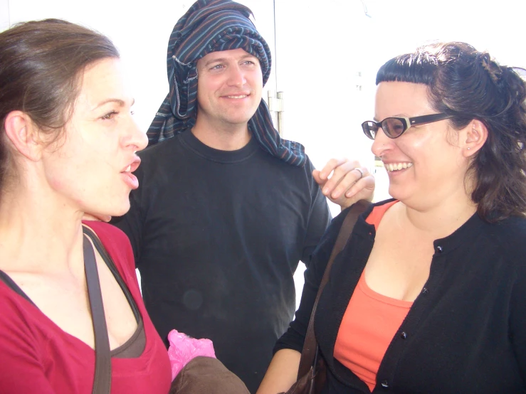 two woman standing next to a man in a black hoodie and red shirt