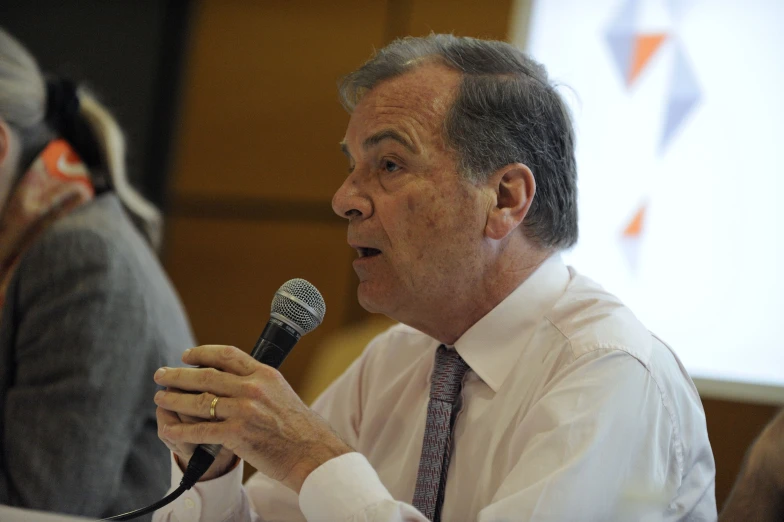 man speaking into microphone while sitting at a table