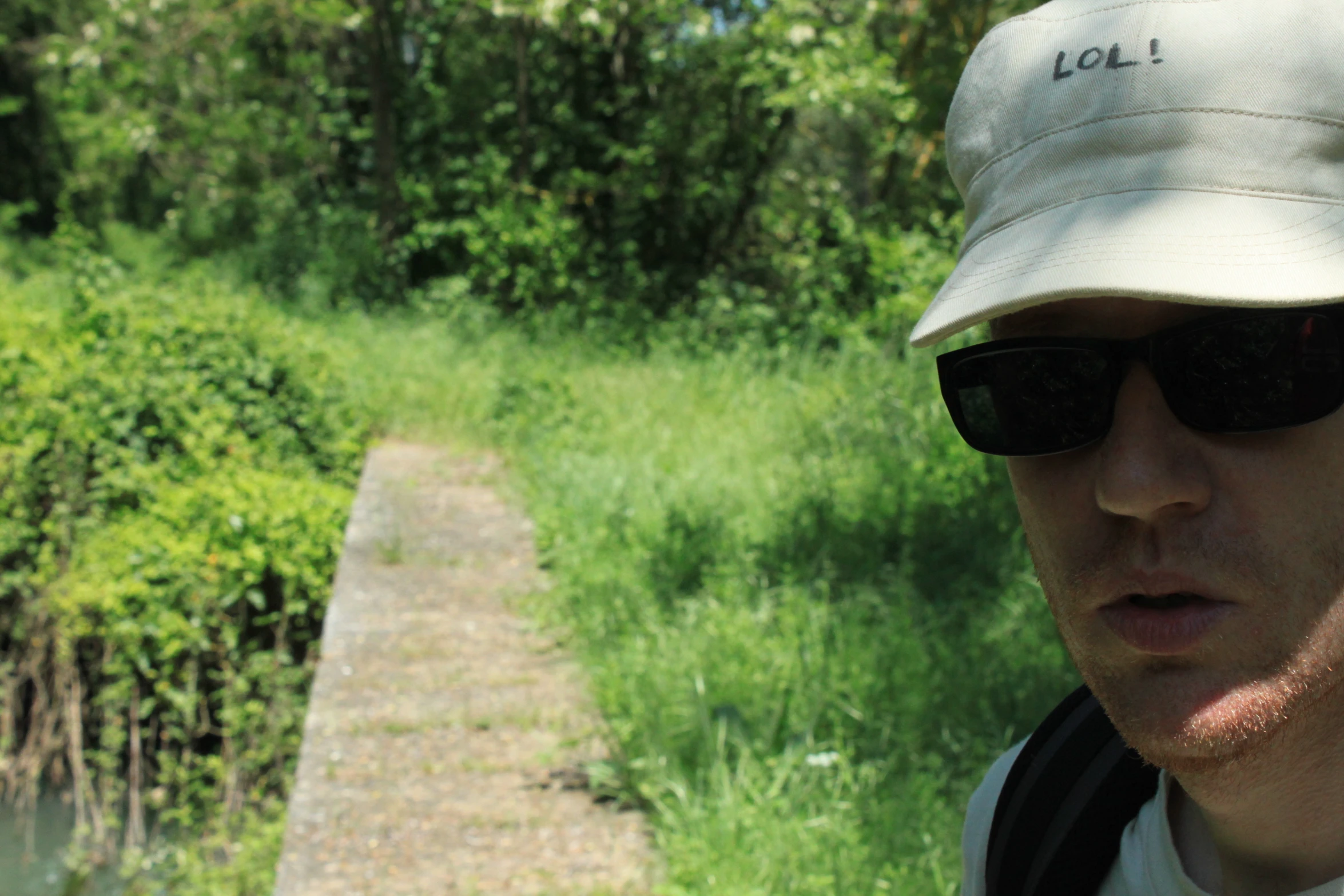 a man wearing a hat and sunglasses looks down the path of a dirt path