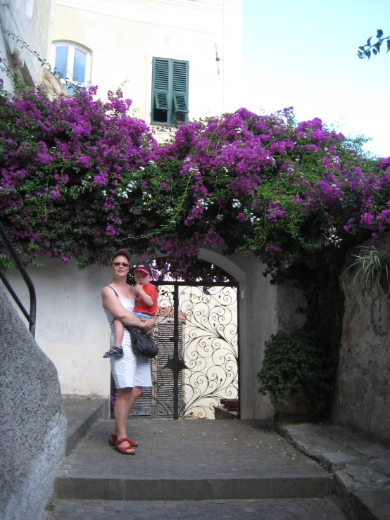 a woman holds her baby while standing in front of a flowering structure