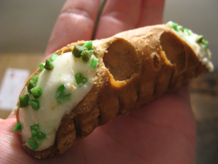 a hand holding a small pastry shaped like a shell