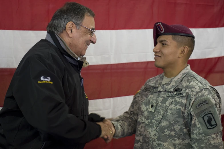 two men in army uniforms shaking hands with a flag behind them